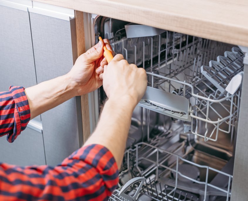 man repairing dishwasher. Male hand with screwdriver installs ki