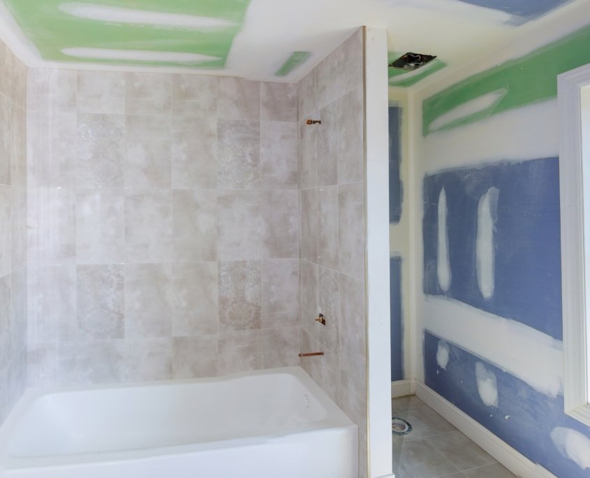 Bathroom remodel progresses as drywall is smoothed, covering seams and screws with tape