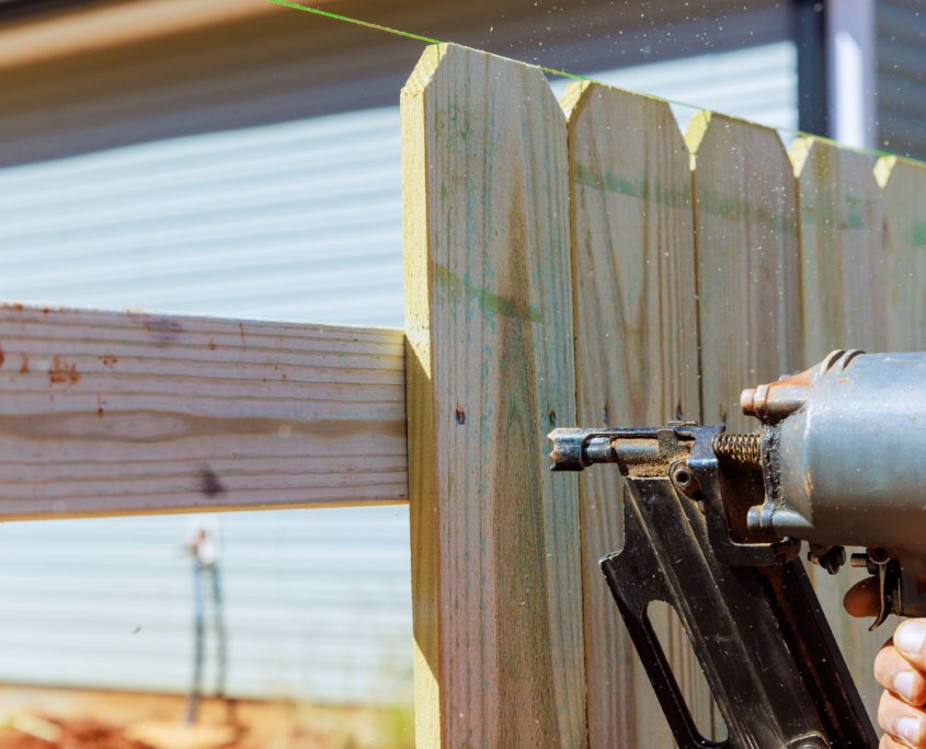 Nailer using air pneumatic gun to secure wooden plank fence during a work