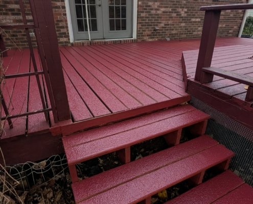 Freshly painted red wooden deck stairs and platform outside a brick house